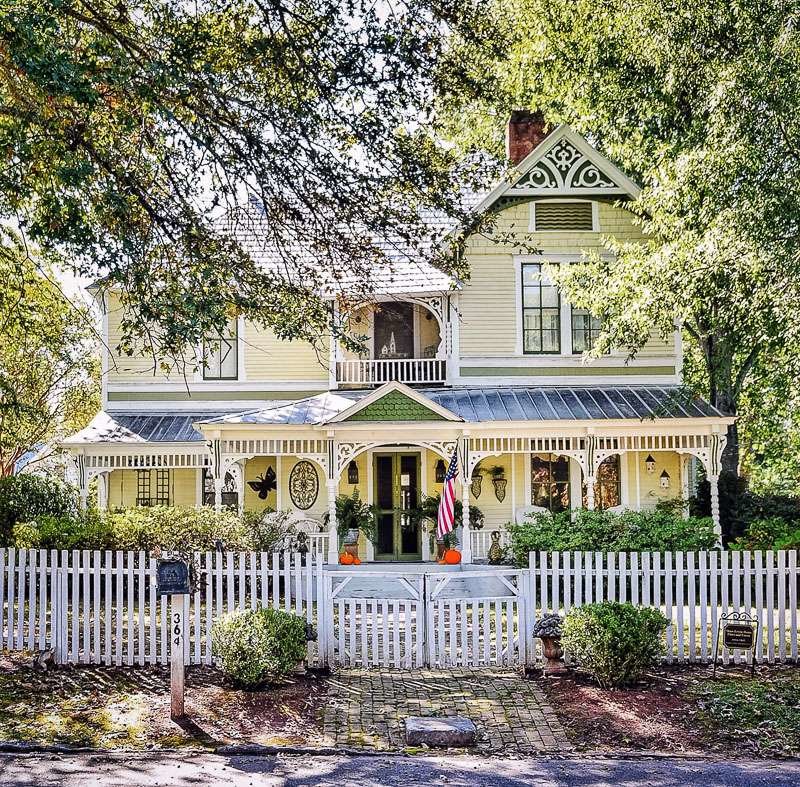 Yellow farmhouse with gingerbread trim, white picket fence and green accents